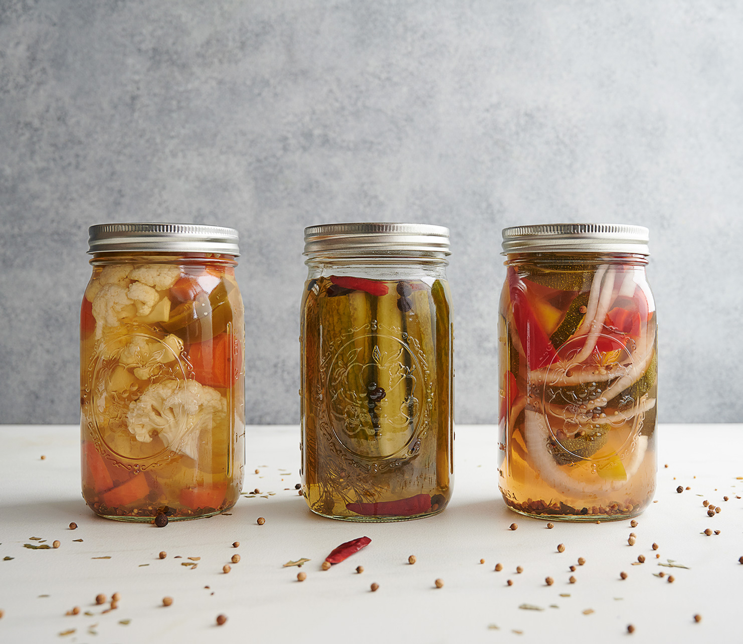 three jars of pickled vegetables on a white counter top