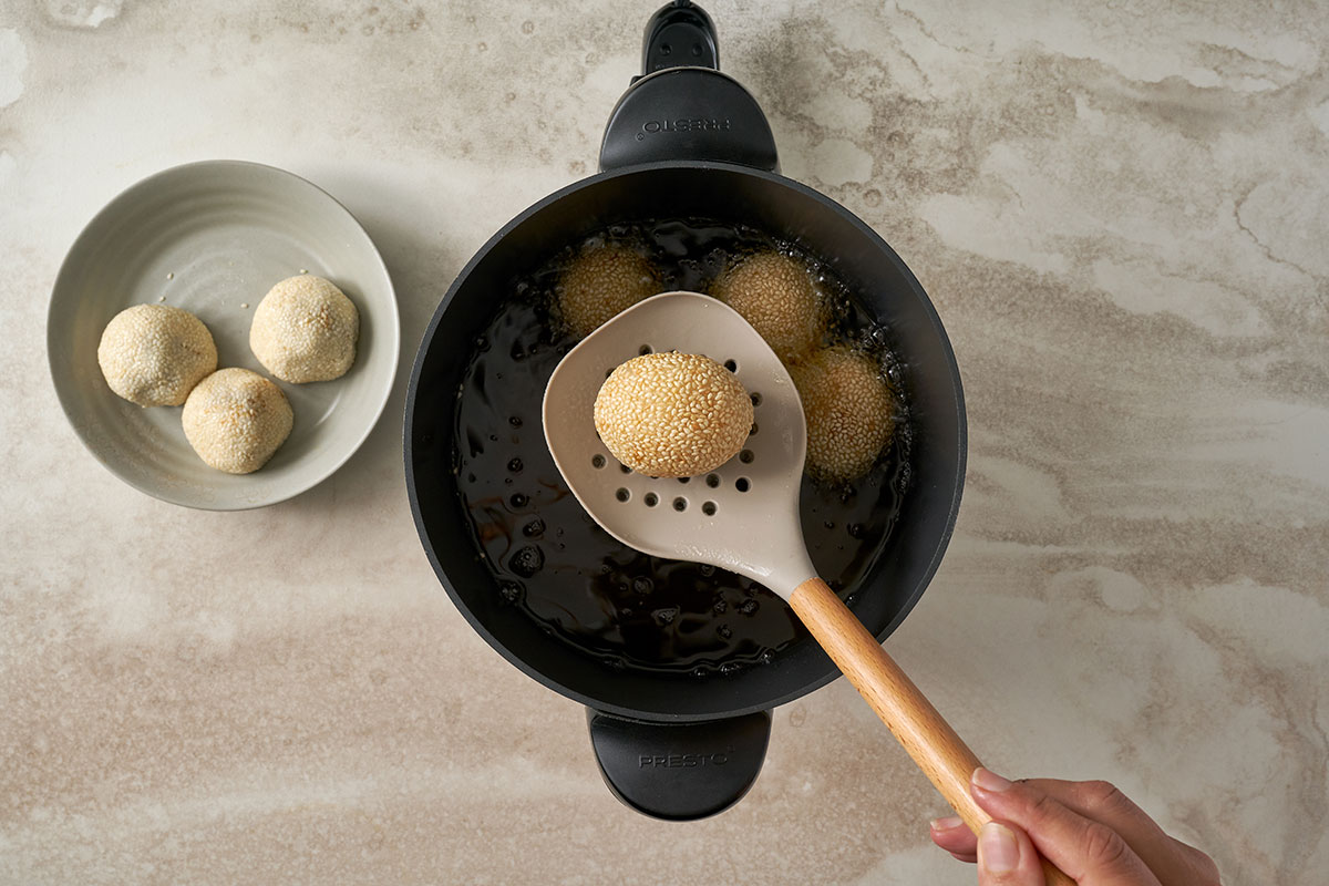 Dipping sesame balls in water, coating with sesame seeds, and frying until crispy and golden brown for Pumpkin Sesame Balls, by Pacific Spice.