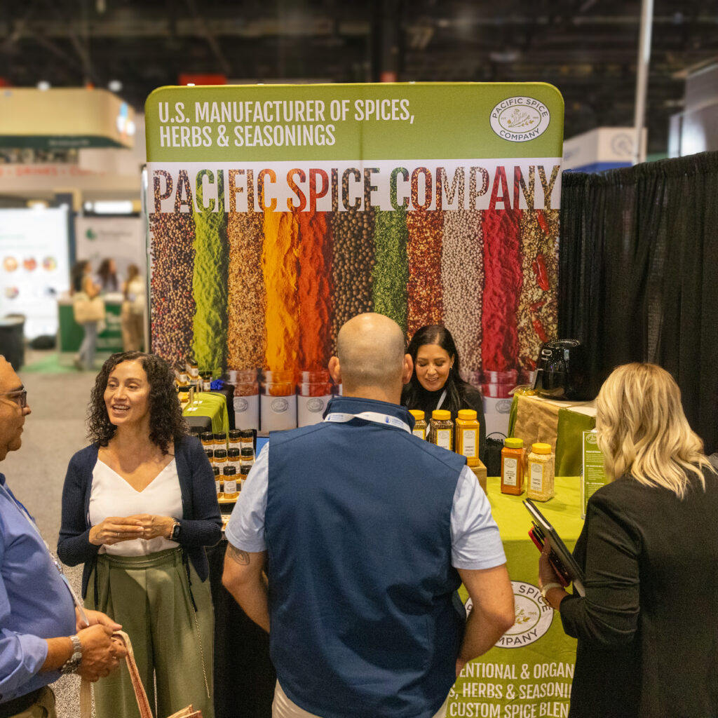 Pacific Spice Company team connecting with food industry professionals at a trade show booth featuring herbs, spices, and custom blends.
