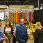 Pacific Spice Company team connecting with food industry professionals at a trade show booth featuring herbs, spices, and custom blends.